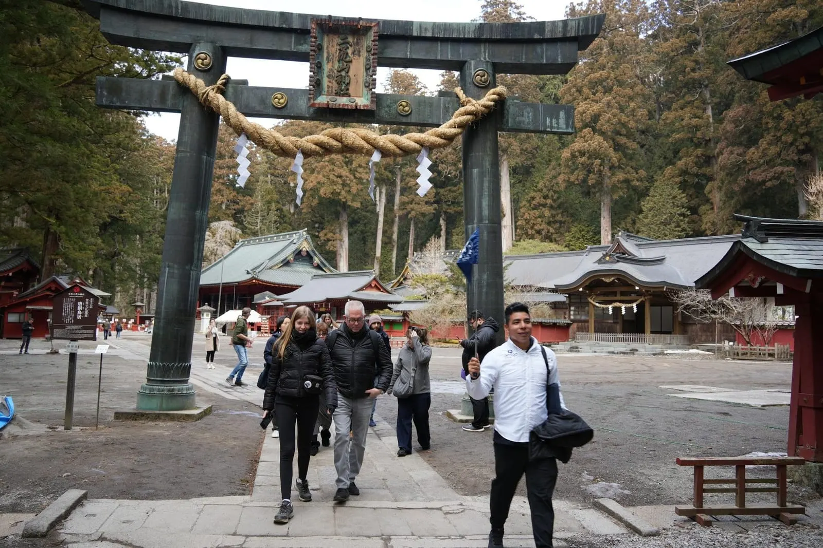 A tour group walking under a bronze torii in the shrine precinct